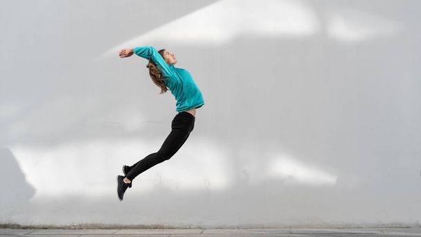Joven chica adulta saltando contra la pared al aire libre
 - Foto, imagen