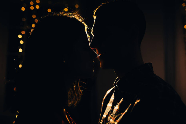 silhouette of a man and a woman on a background of lights in the dark, contour of the face, a kissing couple in the lights of the holiday, love and romance. New Year's Eve and Christmas. - Photo, image