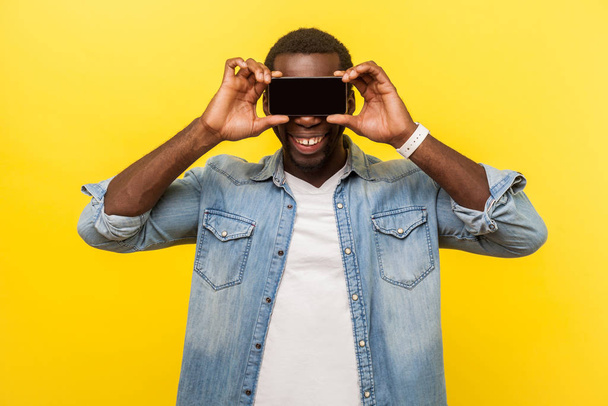 Portrait of positive cheerful man covering eyes with cellphone h - Fotó, kép