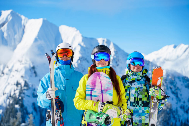 Photo of happy sports woman and men with skis and snowboard standing at ski resort - Photo, Image