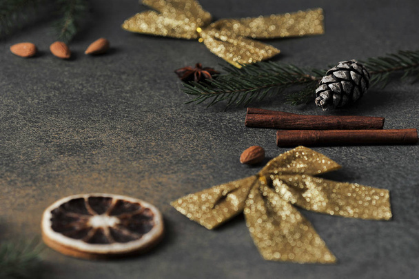 Christmas composition for placing text. Almonds, anise, pine cone, spruce branch, orange, golden bow, cinnamon sticks on a dark background. Close-up. - Fotó, kép