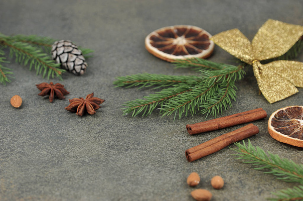 Christmas composition for placing text. Almonds, anise, pine cone, spruce branch, orange, golden bow, cinnamon sticks on a dark background. Close-up. - Φωτογραφία, εικόνα