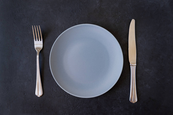 1 empty grey plate, knife, fork on black background, top view, - Foto, Imagen
