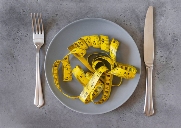 yellow measuring tape on a dark gray plate on a gray background, - Foto, Bild