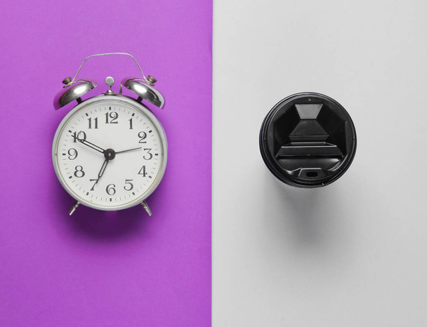 Relógio despertador, recipiente com café em fundo cinza roxo. Vista superior
 - Foto, Imagem