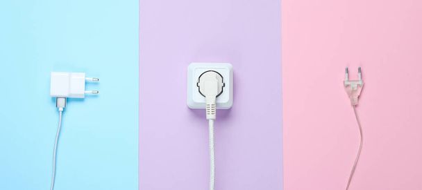 The concept of electrical dependence. Lots of power plugs near power outlets on pastel background - Фото, изображение