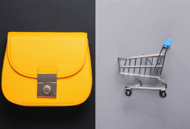 Минималистическая шопоголическая концепция. Желтая кожаная сумка, мини-тележка для покупок на бумажном фоне. Вид сверху - Фото, изображение