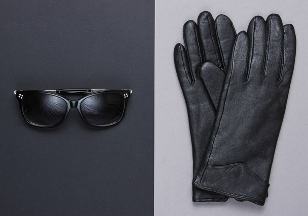 Los accesorios a la moda femeninos. Gafas de sol, guantes negros de cuero sobre un fondo de papel. Vista superior, minimalismo
 - Foto, imagen
