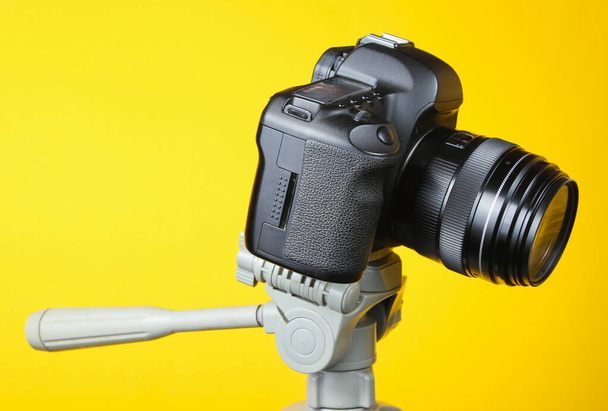 Fotocamera digitale moderna con treppiede su sfondo giallo
 - Foto, immagini