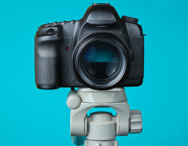 Современная цифровая камера с штативом на синем фоне. Вид спереди
 - Фото, изображение