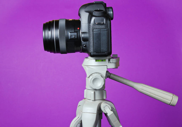 Сучасна цифрова камера з триногом на фіолетовому фоні. Вид спереду
 - Фото, зображення