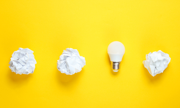 Ampoule à économie d'énergie et boules de papier froissées sur fond jaune. Concept d'entreprise minimaliste, idée. Vue du dessus - Photo, image