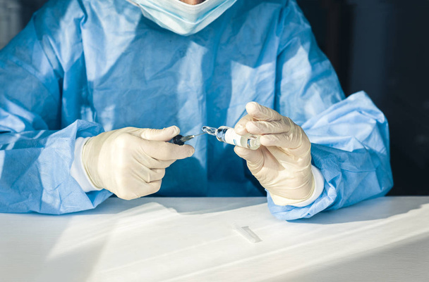 doctor in a blue surgical gown and mask holds in his hand a medi - Fotoğraf, Görsel