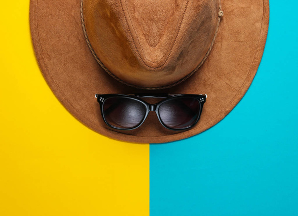 Шляпа с солнцезащитными очками на цветном фоне. Модные сезонные аксессуары - Фото, изображение