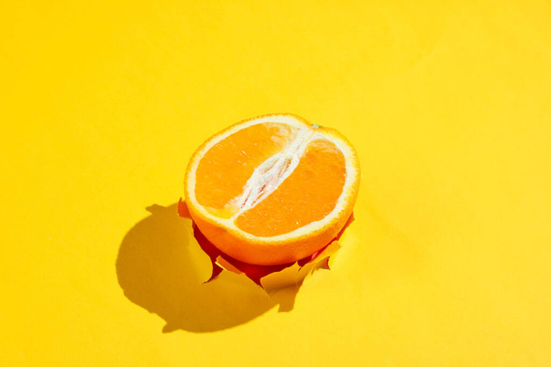 Demi-orange à travers trou déchiré dans du papier jaune. Concept minimaliste des fruits
 - Photo, image
