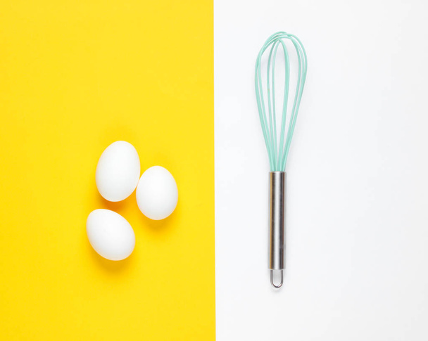 Keittiön vispilä, kananmunia pastellivärillä taustalla. Yläkuva - Valokuva, kuva