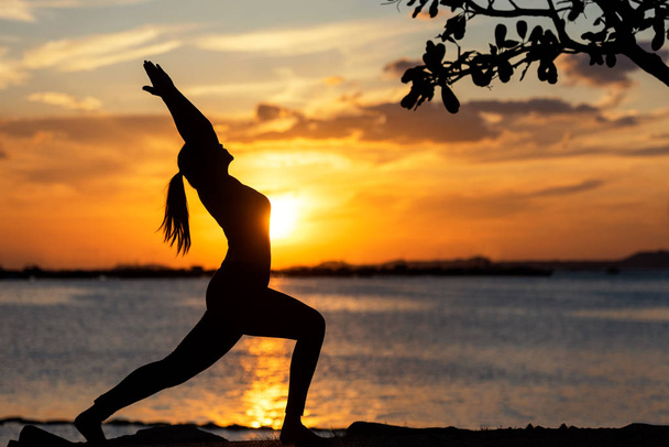 Silhouet gezonde vrouw levensstijl uitoefening van vitale mediteren en het beoefenen van yoga op de rots in strand bij zonsondergang. Gezonde Concept.  - Foto, afbeelding