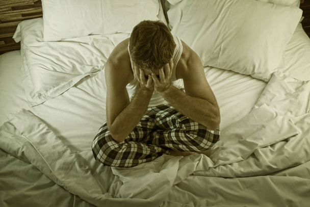 dramatic lifestyle portrait of young attractive sad and depressed man sitting on bed at night feeling stressed and desperate suffering depression problem in sadness and pain - Photo, image