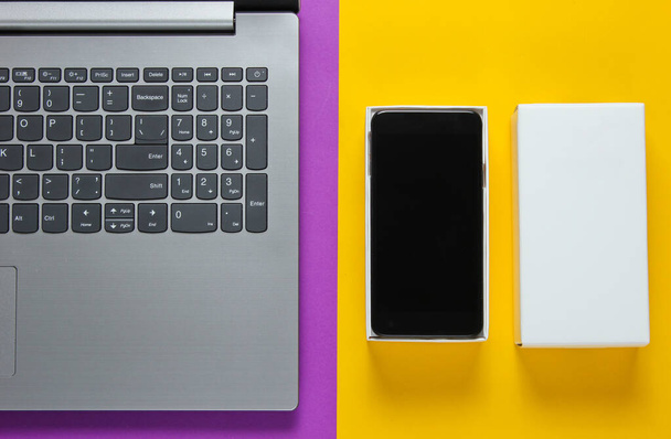 Le concept de déboxe, de blogging techno. Boîte avec un nouveau smartphone, ordinateur portable sur fond jaune violet. Vue du dessus
 - Photo, image