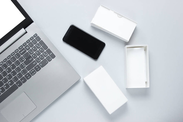 Boksu açma, tekno blog yazma kavramı. Yeni akıllı telefonlu bir kutu, gri arka planda bir laptop. Üst görünüm - Fotoğraf, Görsel