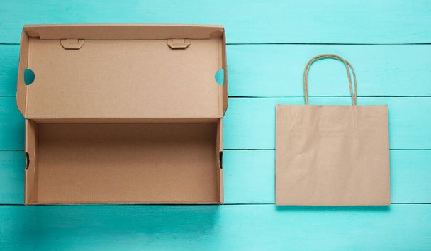 Empty cardboard box and paper bag on blue wooden background. Ecology concept.  Top view - Photo, Image
