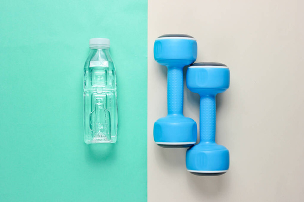 Minimalist fitness konsepti. Dambıllar, renkli arka planda bir şişe su. Üst görünüm - Fotoğraf, Görsel
