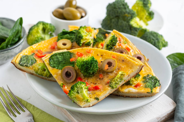 Omelette con broccoli, spinaci e olive su un piatto. Frittata - frittata italiana con verdure verdi
. - Foto, immagini