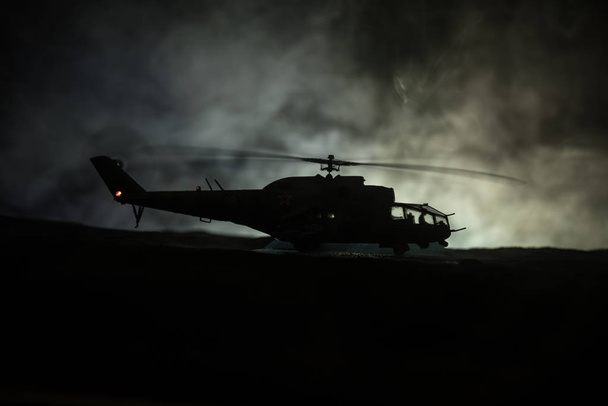 Silhouette of military helicopter ready to fly from conflict zone. Decorated night footage with helicopter starting in desert with foggy toned backlit. Selective focus. - Фото, зображення