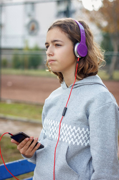 Young beautiful fashionable teenager girl listens to music on headphones from a smartphone - Foto, Imagem