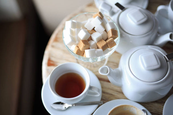 Bir fincan çay, ahşap masanın kenarında durur, şeker kasesinde kare şeker, çaydanlık, kahve ısıtıcısı - Fotoğraf, Görsel