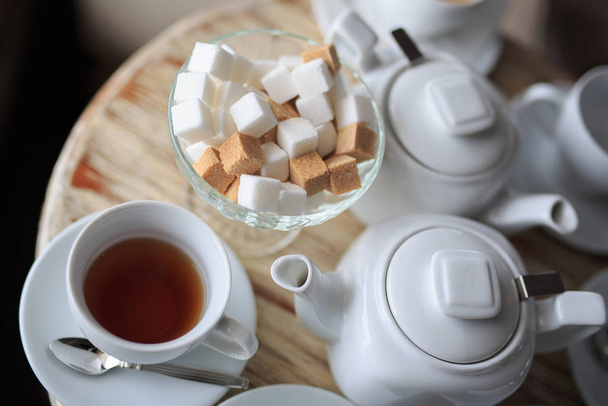 Bir fincan çay, ahşap masanın kenarında durur, şeker kasesinde kare şeker, çaydanlık, kahve ısıtıcısı - Fotoğraf, Görsel