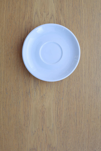 jeden čistě bílý keramický talíř stojí na dřevěném stole - Fotografie, Obrázek