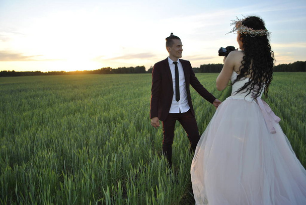 Wedding couple on a photo shoot in a wheat field. The bride shoots the groom on the camera against the sunset. - Photo, image