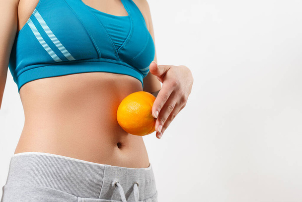 a young woman in sportswear holds an orange on her stomach - Фото, зображення