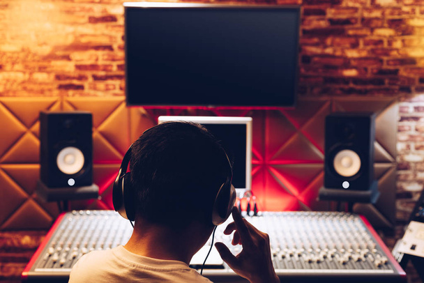 back of asian male music producer working on audio mixing console in recording studio. music production, broadcasting, post production concept - Photo, image