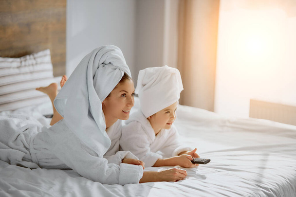 portrait of lovely mother and daughter on bed with tv remote - Photo, Image