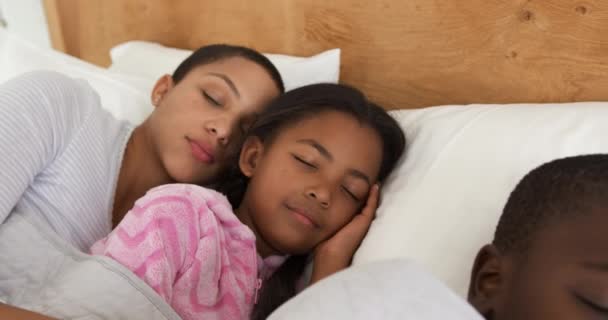 Front view close up of an African American woman and her young son and daughter lying asleep together in a row in her bed, slow motion - Záběry, video