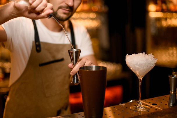 Bartender pours cocktail with bar spoon and jigger - Fotó, kép
