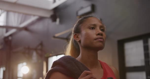 Low angle front view close up of an athletic mixed race woman wearing sports clothes cross training at a gym walking in the gym holding a towel - Video, Çekim