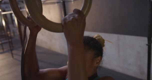 Вид сбоку на атлетическую смешанную расовую женщину в спортивной одежде, тренирующуюся в спортзале, поднимающуюся на тренировочных кольцах, замедленную съемку
 - Кадры, видео