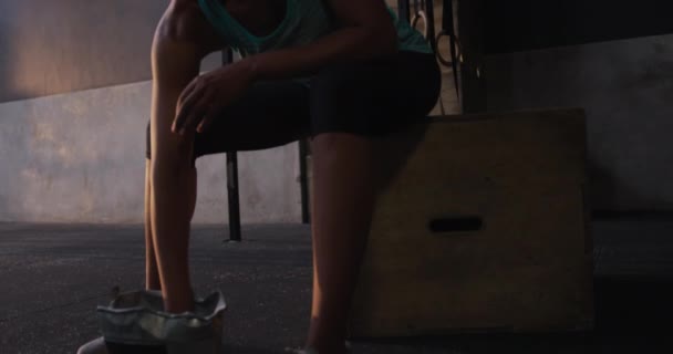 Side view of an athletic mixed race woman wearing sports clothes cross training at a gym, sitting and rubbing chalk in her hands in preparation for lifting weights, slow motion - Felvétel, videó
