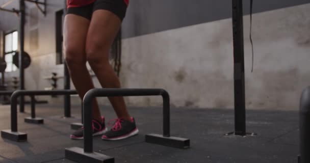 Side view close up of an athletic mixed race woman wearing sports clothes cross training at a gym jumping sideways over low hurdles, slow motion - Filmmaterial, Video
