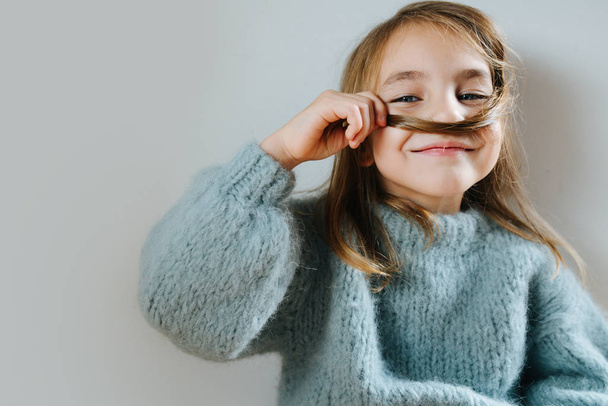 Petite fille dans un pull bleu jouant avec ses cheveux, faisant de fausses moustache
 - Photo, image