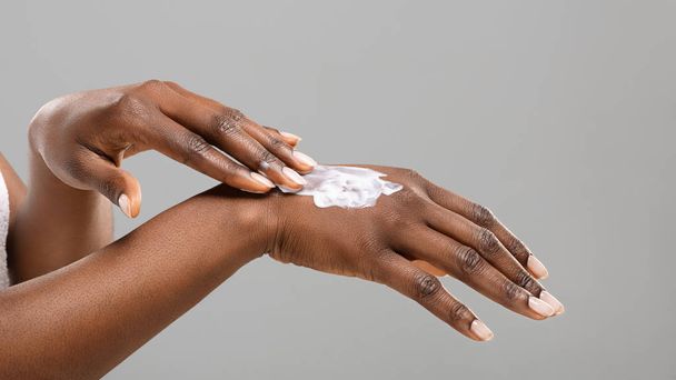Mulher negra aplicando loção corporal em suas mãos
 - Foto, Imagem