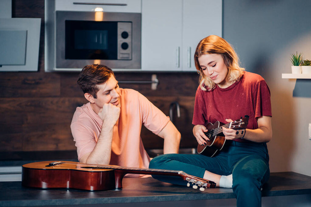 young caucasian woman playing ukulele while his friend listen to her at home - Fotó, kép