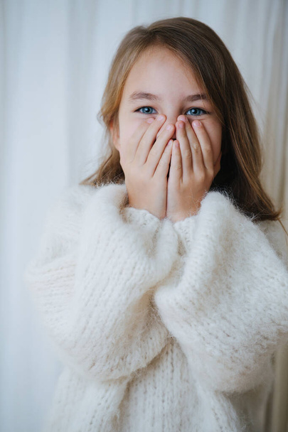 Portrait of a playful little girl in white fluffy knitted sweater covering face - Foto, afbeelding