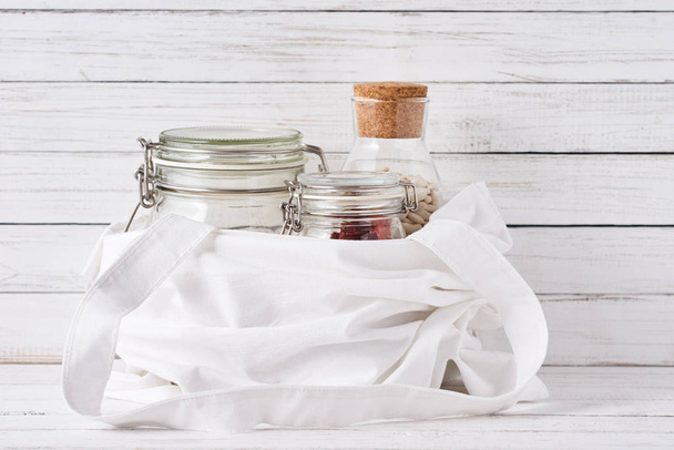 Glass jar, wooden brush and shopping bag on a white background.  - Фото, изображение