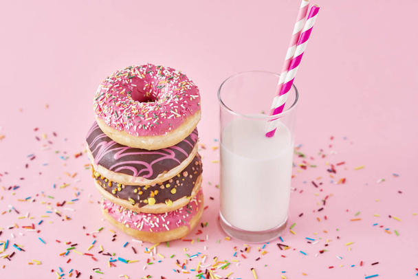 Hromada barevných koblih zdobené a sklenice mléka na růžovém pozadí - Fotografie, Obrázek