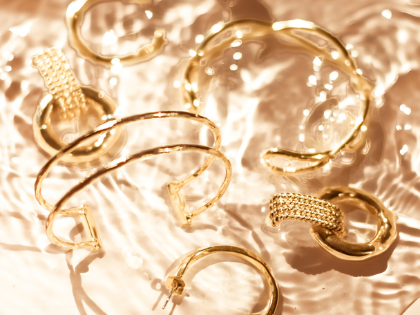 Golden bracelets, earrings, rings, jewelery on gold water backgr - Zdjęcie, obraz