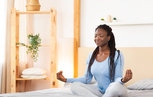 Békés afro hölgy ül meditál az ágyban otthon - Fotó, kép